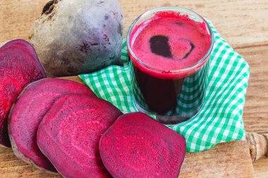 Bardakta taze pancar suyu ve tahta tahtada dilimlenmiş pancar kökü ve peçete.