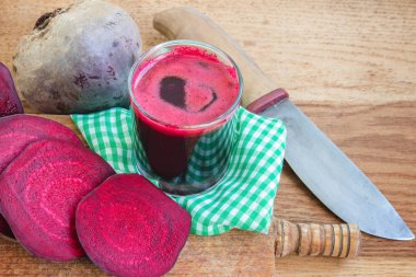 Bardakta taze pancar suyu ve tahta tahtanın üzerinde bıçak ve peçeteyle dilimlenmiş pancar kökü.