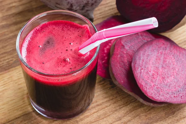 Bardakta taze pancar suyu ve tahta masada dilimlenmiş pancar kökü.
