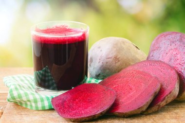 Bardakta taze pancar suyu ve tahta masada dilimlenmiş pancar kökü bulanık, dağılmış, doğa arka planı.