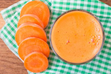 Bardakta taze havuç suyu ve peçetede dilimlenmiş havuç, yakın plan, üst manzara.