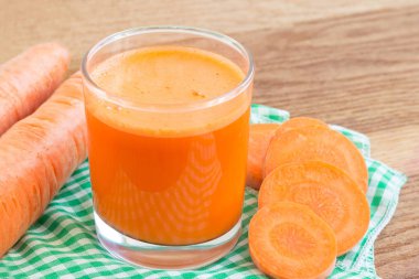 Bardakta taze havuç suyu ve tahta masada peçetede kesilmiş havuç sebzesi.