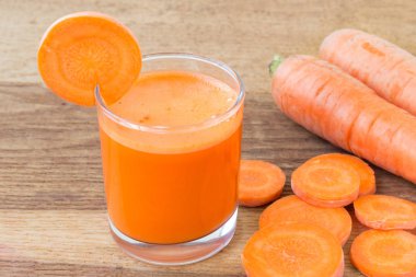 Bardakta taze havuç suyu ve tahta masada dilimlenmiş havuç sebzesi.