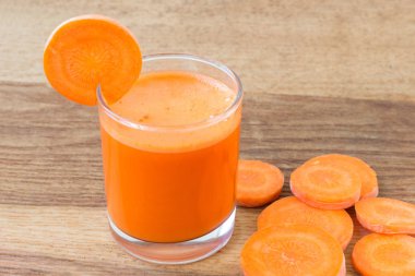 Bardakta taze havuç suyu ve tahta masada dilimlenmiş havuç sebzesi.