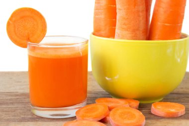 Bardaktaki taze havuç suyu, dilimler ve havuçlar ahşap masada sarı kâsede sebze, beyaz arka plan.