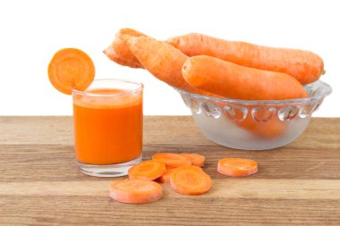 Taze havuç suyu bardakta, dilimler ve havuçlar kasede sebzeler tahta masada, beyaz arka plan