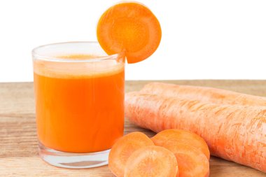 Bardakta taze havuç suyu ve tahta masada havuç dilimleri, beyaz arka plan.