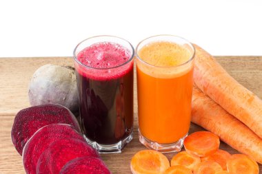 İki bardak taze pancar ve havuç suyu, pancar kökü ve havuç, ahşap masada sebze, beyaz arka plan.