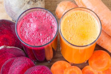 İki bardak taze pancar, havuç suyu, pancar kökü ve havuç, ahşap masada sebze.