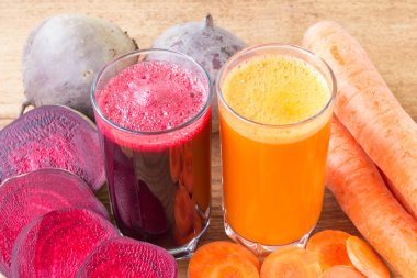 İki bardak taze pancar, havuç suyu, pancar kökü ve havuç, ahşap masada sebze.