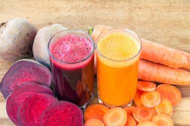 İki bardak taze pancar, havuç suyu, pancar kökü ve havuç, ahşap masada sebze.