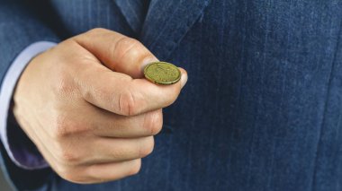 Mavi takım elbiseli bir işadamı elinde altın euro sent tutuyor, yazı tura atıyor, yazı tura atıyor.
