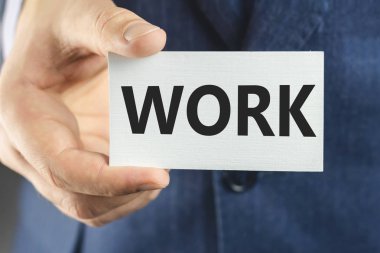 Mavi takım elbiseli bir iş adamı, el kamerasıyla metin yazan bir kart gösteriyor.