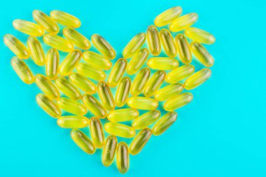 Bir sürü sarı kapsül omega 3, yağ asidi, mavi arka planda kalp şeklinde balık yağı.