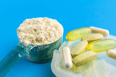 Protein tozu ölçme plastik kaşık ve karmaşık vitamini, omega 3, glukozamin kapsül, içinde mavi arka plan üzerinde takviyeleri, Spor beslenme.