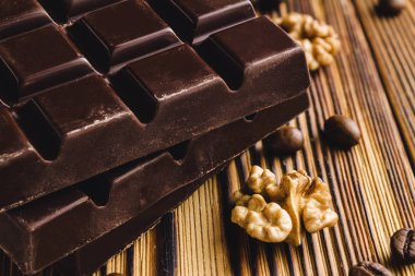 Üç parça acı, koyu çikolata, ceviz çekirdeği ve ahşap arka planda kahve çekirdeği, yakın çekim manzarası..