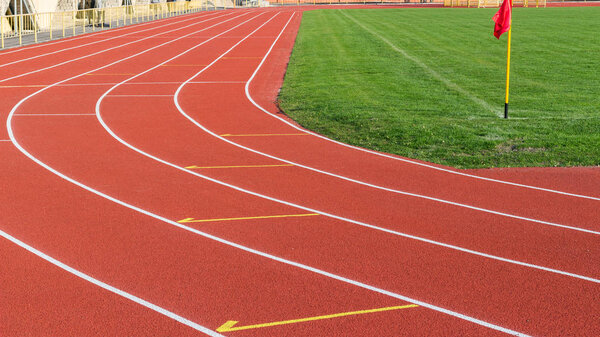 Red running track and white lanes on sport stadium.