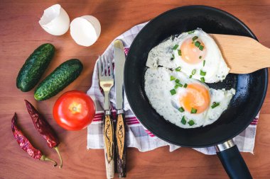 Tavada yumurta, salatalık, domates ve ahşap arka planda kırmızı biber..