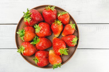 Beyaz ahşap zemin üzerinde kahverengi tabakta taze organik çilek hasat edin..