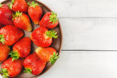 Beyaz ahşap zemin üzerinde kahverengi tabakta taze organik çilek hasat edin..