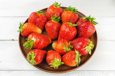 Beyaz ahşap zemin üzerinde kahverengi tabakta taze organik çilek hasat edin..