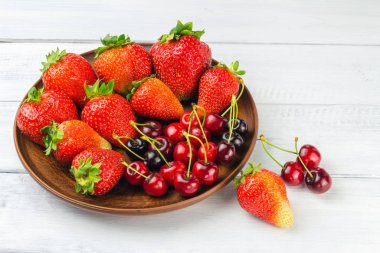 Taze organik böğürtlen, çilek ve kiraz hasadı beyaz ahşap zemin üzerinde kahverengi tabakta.