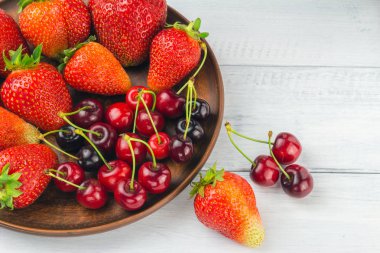 Taze organik böğürtlen, çilek ve kiraz hasadı beyaz ahşap zemin üzerinde kahverengi tabakta.