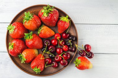 Taze organik böğürtlen, çilek ve kiraz hasadı beyaz ahşap zemin üzerinde kahverengi tabakta, üst manzara.