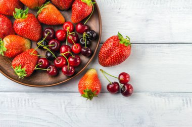 Taze organik böğürtlen, çilek ve kiraz hasadı beyaz ahşap zemin üzerinde kahverengi tabakta, üst manzara.