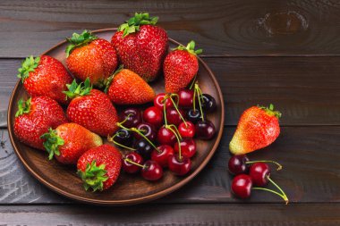 Taze organik böğürtlen, çilek ve kirazları koyu ahşap zemin üzerinde kahverengi tabakta toplayın..