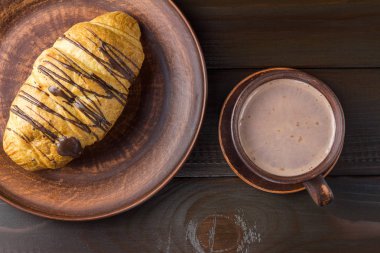 Sıcak çikolata ya da bardakta kakao ve tabakta tatlı kruvasan, koyu kahverengi ahşap masa, üst manzara..