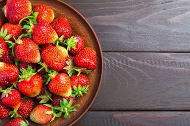Kahverengi tabakta taze organik çilekler. Koyu ahşap zemin üzerinde. Üst manzara..