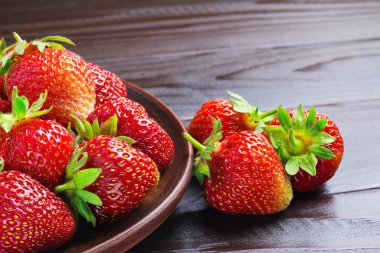 Koyu ahşap zemin üzerinde kahverengi tabakta taze organik çilekler, yakın çekim görüntüsü..