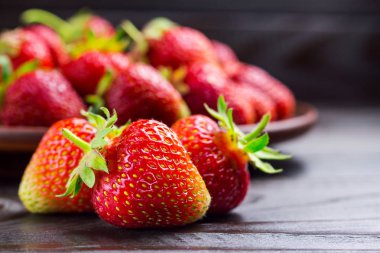 Koyu ahşap zemin üzerinde kahverengi tabakta taze organik çilekler, yakın çekim görüntüsü..