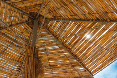 Mavi ve bulutlu arka planda saman plaj şemsiyesi altında görünüm.