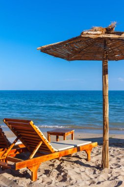 Denizde kumsalda iki güneşlik ve saman şemsiye, yaz mevsimi deniz istirahatı konsepti..