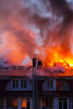Şehrin çatısı dumanla alev alev yanıyor. İtfaiyeci ya da itfaiyeci yangını söndürüyor..