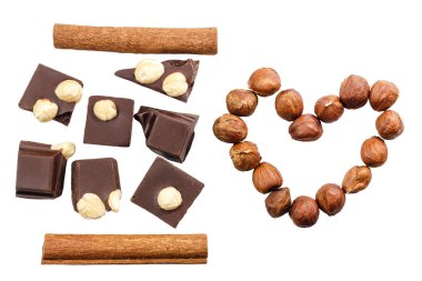 Tarçın çubuklu acı siyah çikolata küpleri ve beyaz arka planda izole edilmiş kalp şeklinde fındık parçaları..