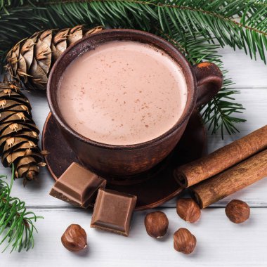 Sütlü sıcak kakao, kırık çikolata küpleri, fındık ve tarçın çubukları, Noel ağacı dalları, beyaz ahşap kalaslarda çam kozalağı.