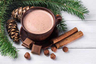 Sütlü sıcak kakao, kırık çikolata küpleri, fındık ve tarçın çubukları, Noel ağacı dalları, beyaz ahşap kalaslarda çam kozalağı.