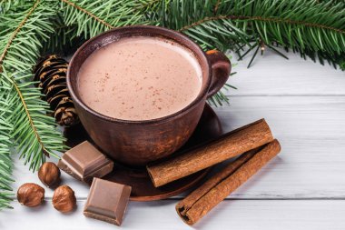 Sütlü sıcak kakao, kırık çikolata küpleri, fındık ve tarçın çubukları, Noel ağacı dalları, beyaz ahşap kalaslarda çam kozalağı.