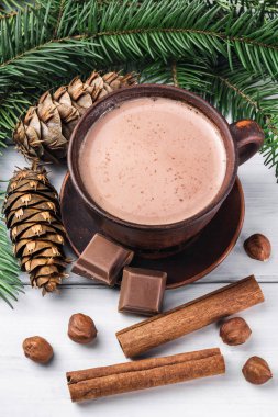 Sütlü sıcak kakao, kırık çikolata küpleri, fındık ve tarçın çubukları, Noel ağacı dalları, beyaz ahşap kalaslarda çam kozalağı.