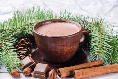 Sütlü sıcak kakao, kırık çikolata küpleri, fındık ve tarçın çubukları, Noel ağacı dalları, beyaz ahşap kalaslarda çam kozalağı.