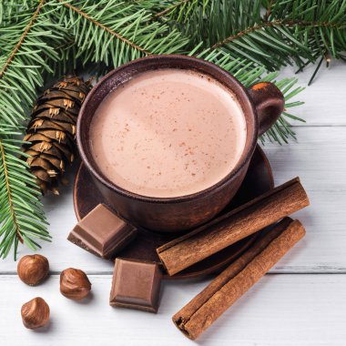 Sütlü sıcak kakao, kırık çikolata küpleri, fındık ve tarçın çubukları, Noel ağacı dalları, beyaz ahşap kalaslarda çam kozalağı.