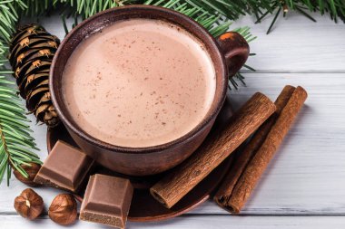 Sütlü sıcak kakao, kırık çikolata küpleri, fındık ve tarçın çubukları, Noel ağacı dalları, beyaz ahşap kalaslarda çam kozalağı.