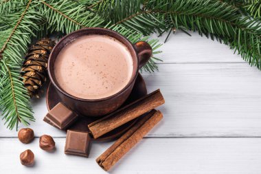 Sütlü sıcak kakao, kırık çikolata küpleri, fındık ve tarçın çubukları, Noel ağacı dalları, beyaz ahşap kalaslarda çam kozalağı.