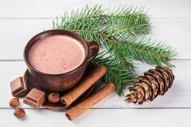 Sütlü sıcak kakao, kırık çikolata küpleri, fındık ve tarçın çubukları, Noel ağacı dalları, beyaz ahşap kalaslarda çam kozalağı.