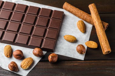 Acı, koyu çikolata bar, badem, fındık ve tarçın sopa ahşap arka plan üzerinde.