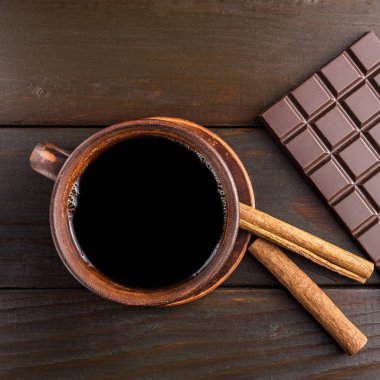 Sıcak siyah kahve kahverengi kil Kupası, koyu çikolata bar ve ahşap zemin, üstten görünüm üzerine tarçın çubuğu.