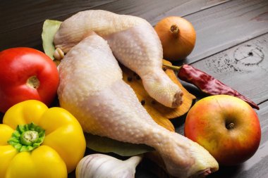 Baharat ve domates, biber, sarımsak, kırmızı biber, soğan, elma, ahşap koyu kahverengi plakalar gibi sebzeler ile kesme tahtası üzerinde iki çiğ tavuk budu.